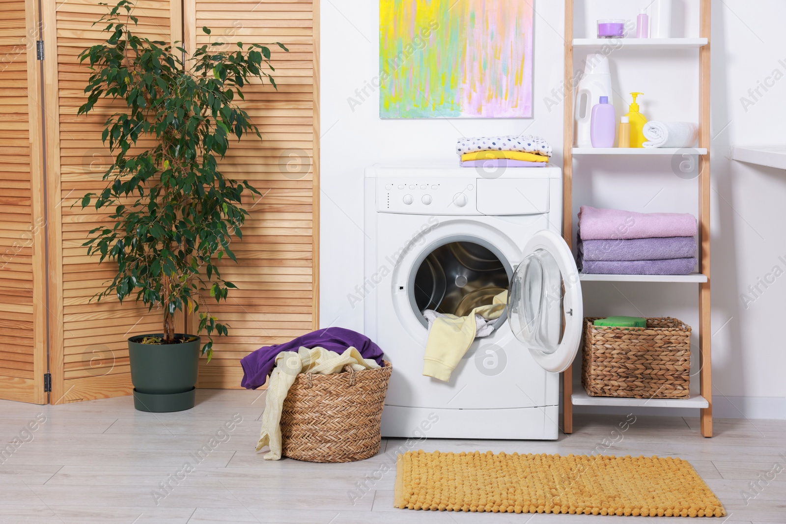 Photo of Washing machine, detergents, clean towels and basket with laundry in room