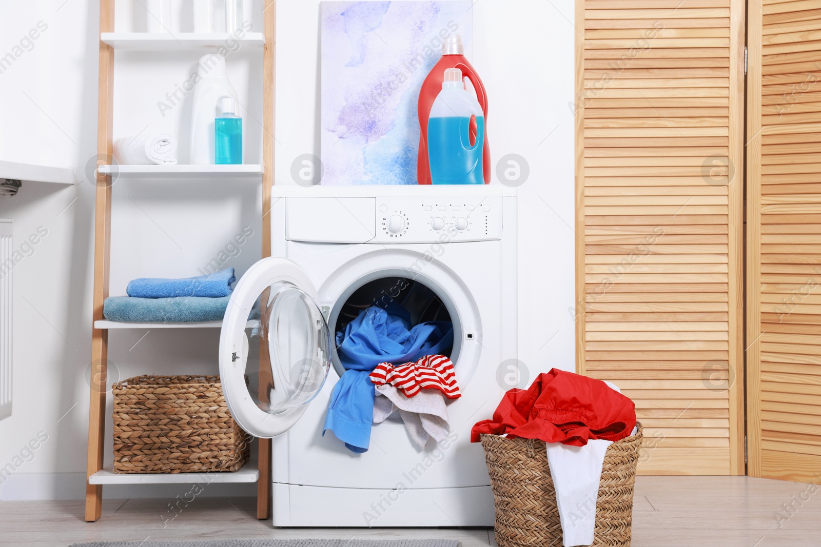 Photo of Washing machine, detergents, clean towels and basket with laundry in room