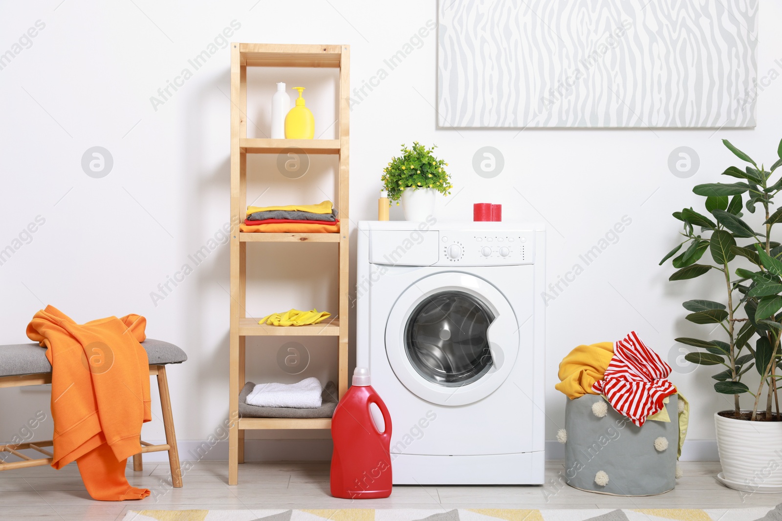 Photo of Washing machine, detergents, basket with laundry and plant in room