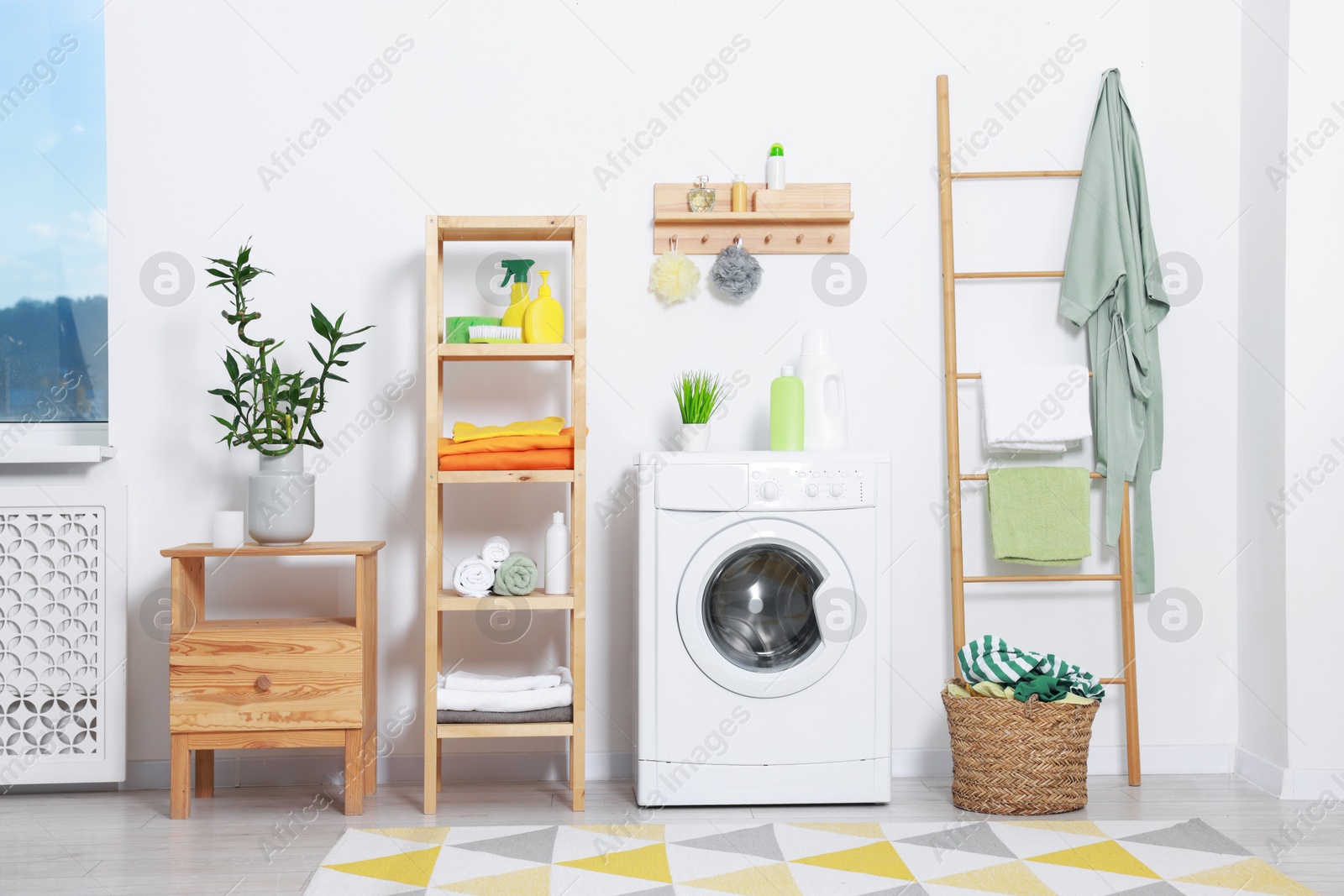 Photo of Washing machine, detergents, bathrobe and basket with laundry in room