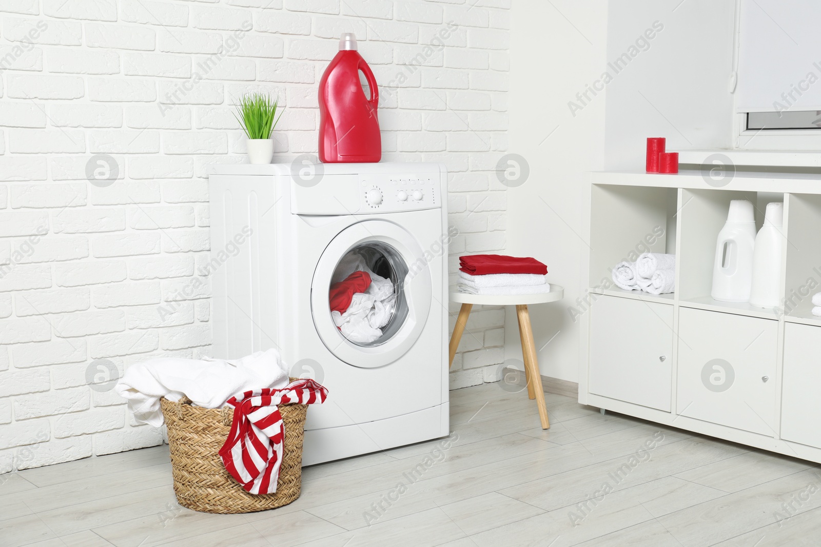 Photo of Washing machine, detergents and basket with laundry in room