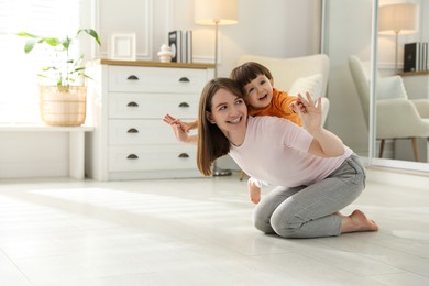 Photo of Happy mother playing with her little son at home. Space for text