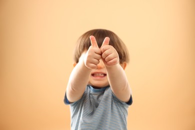 Smiling little boy showing thumbs up on beige background, selective focus