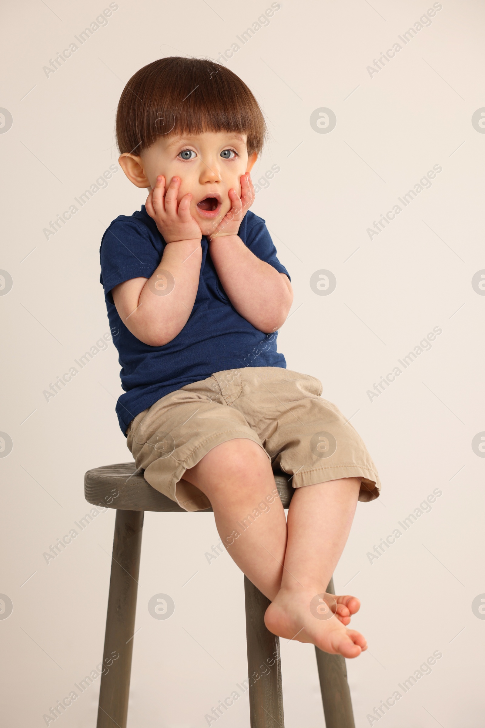 Photo of Emotional little boy sitting on stool against light grey background