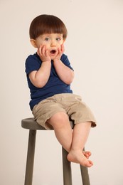 Photo of Emotional little boy sitting on stool against light grey background