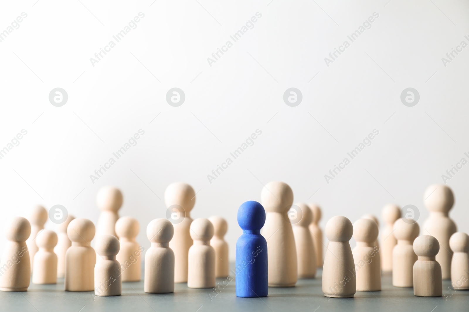 Photo of Human resources concept. Blue figure among wooden ones on table against light background, closeup. Space for text