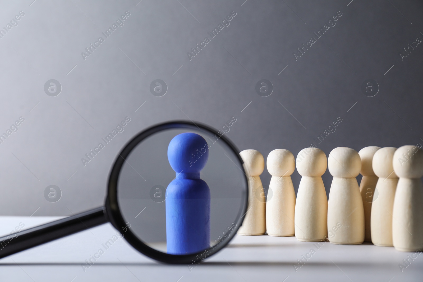 Photo of Human resources concept. Looking at blue figure through magnifying glass on table against grey background, closeup. Space for text