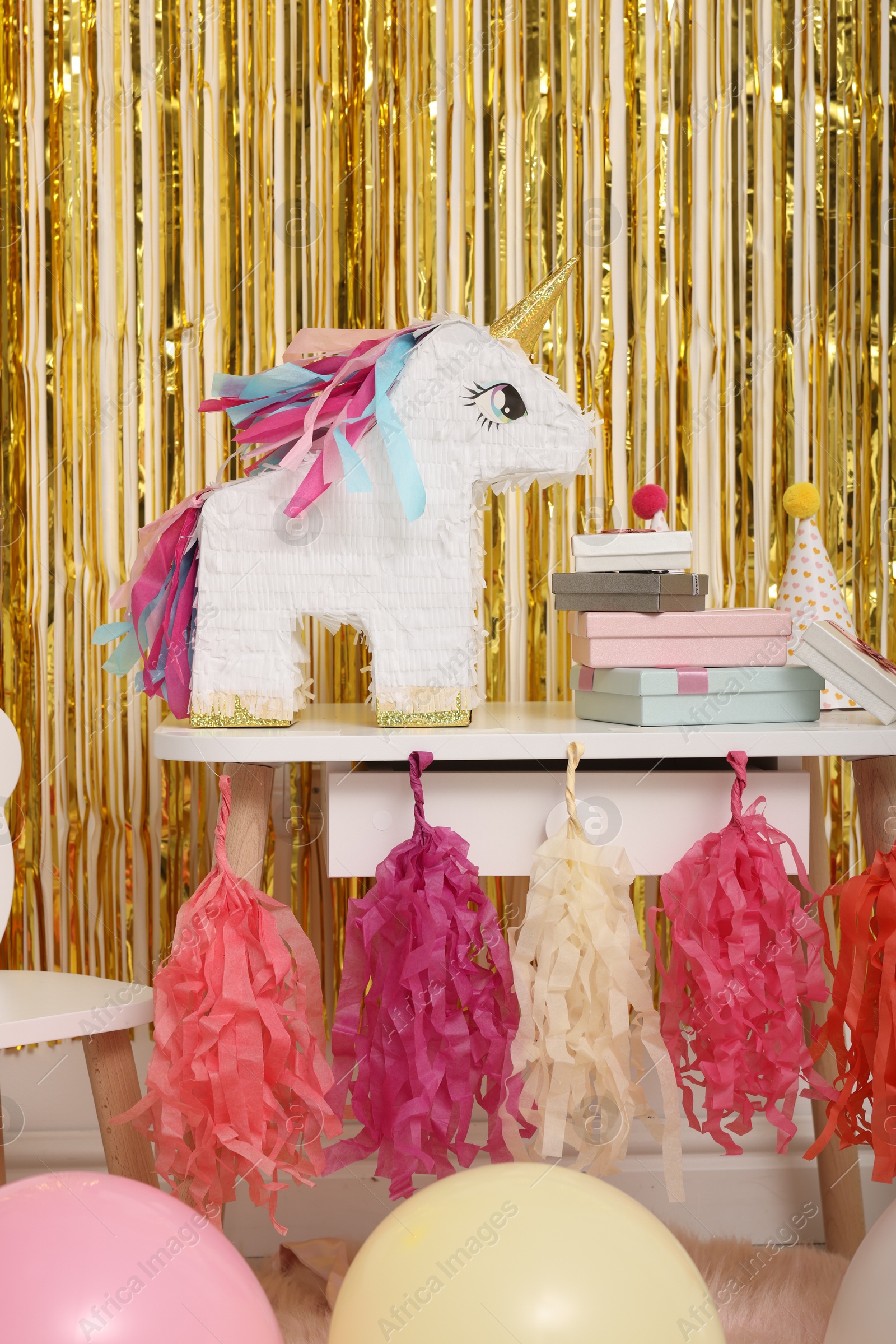 Photo of Bright pinata in shape of unicorn and party accessories against foil fringe curtain indoors