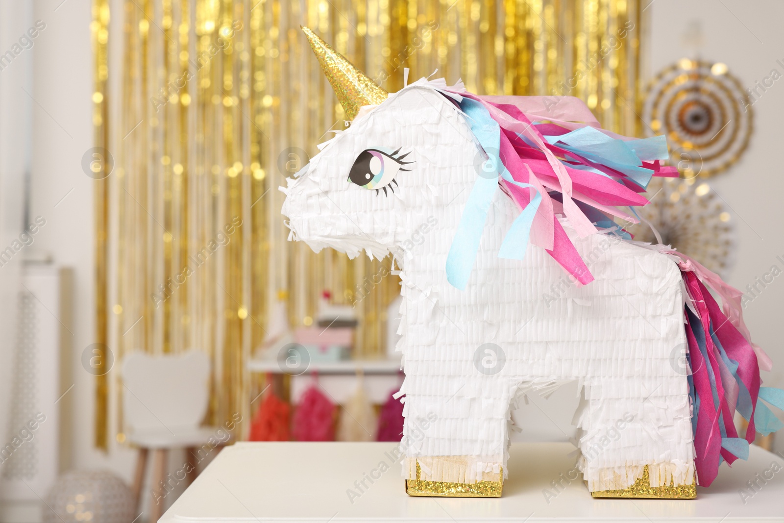 Photo of Bright pinata in shape of unicorn on white table in festive decorated room, space for text