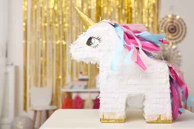 Photo of Bright pinata in shape of unicorn on white table in festive decorated room, space for text