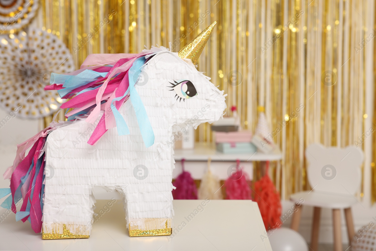 Photo of Bright pinata in shape of unicorn on white table in festive decorated room, space for text