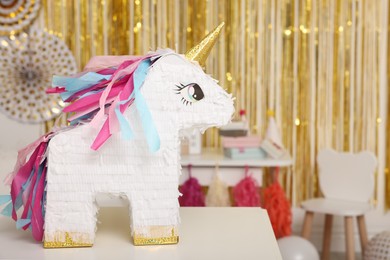 Photo of Bright pinata in shape of unicorn on white table in festive decorated room, space for text