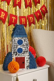 Photo of Bright pinata in shape of rocket and party accessories in festive decorated room