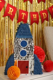 Photo of Bright pinata in shape of rocket and party accessories in festive decorated room