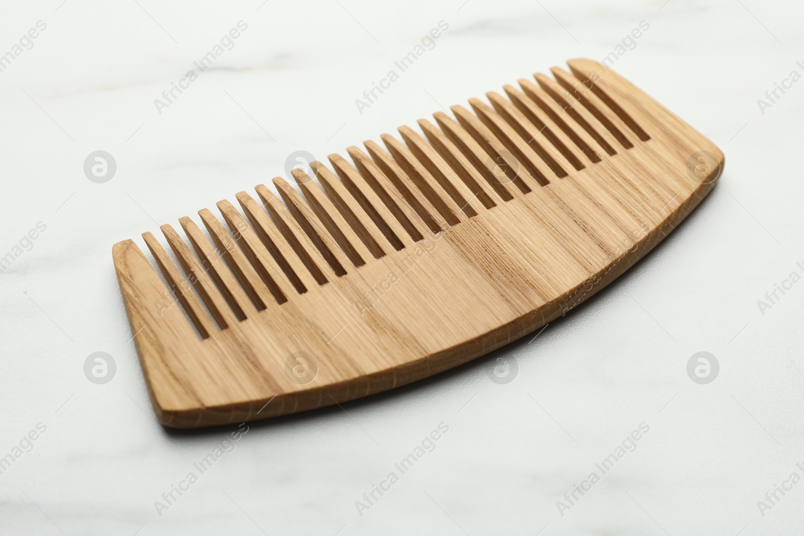 Photo of One wooden hair comb on white marble table, closeup