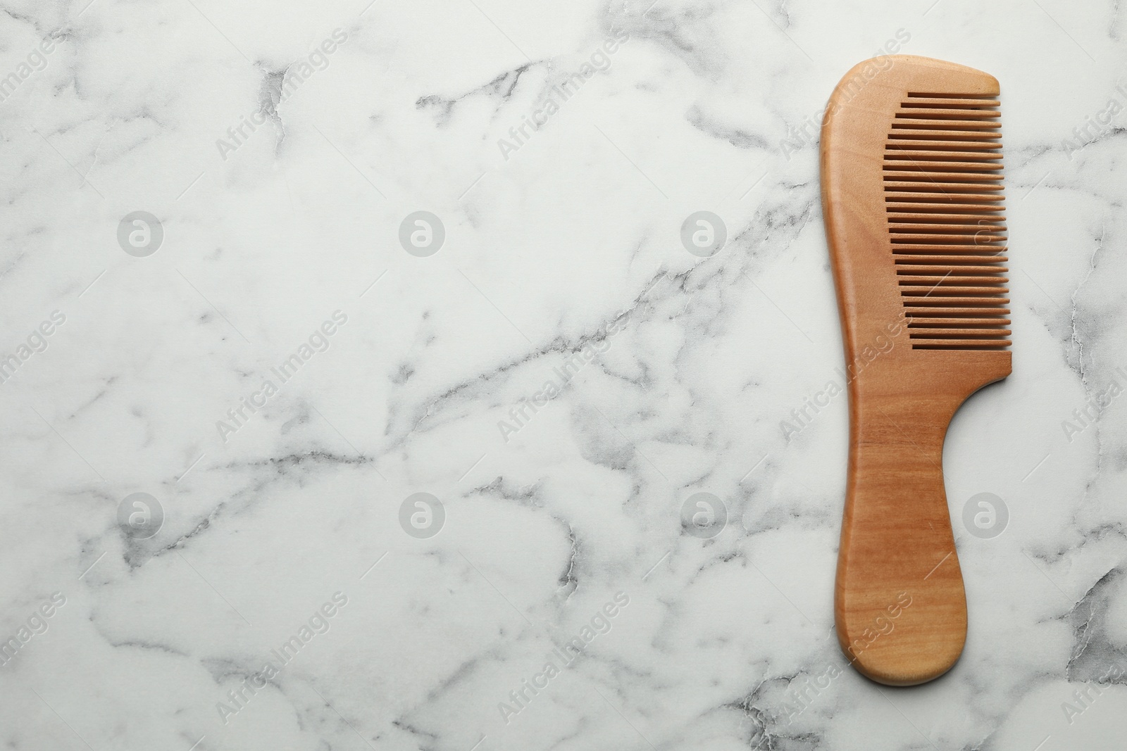 Photo of One wooden hair comb on white marble table, top view. Space for text