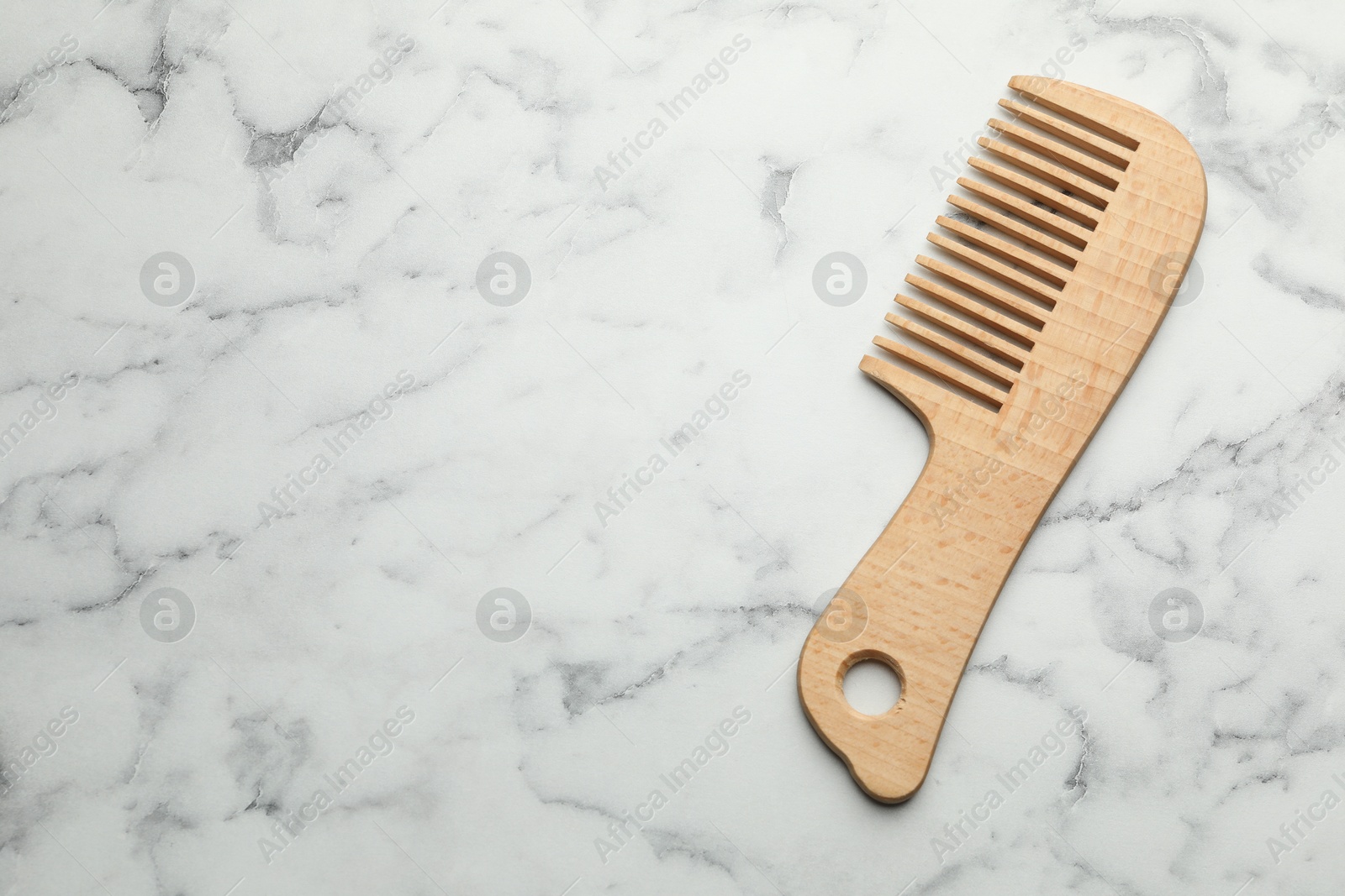 Photo of One wooden hair comb on white marble table, top view. Space for text