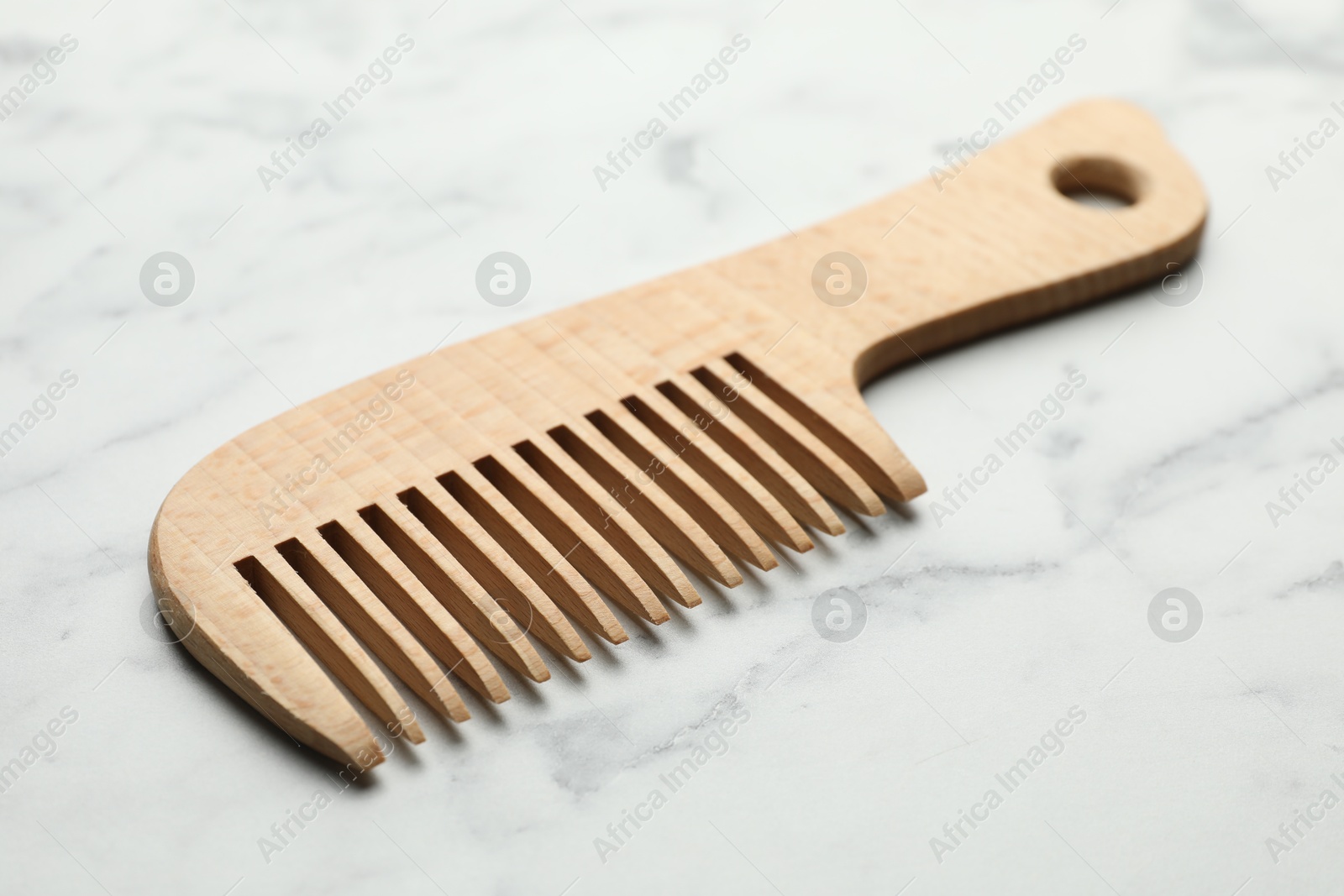 Photo of One wooden hair comb on white marble table, closeup