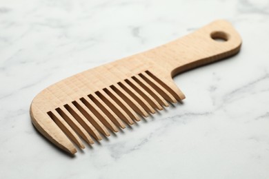 Photo of One wooden hair comb on white marble table, closeup