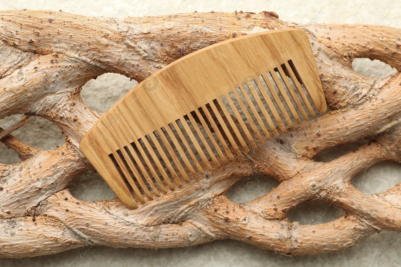 Photo of One wooden hair comb and tree branch on beige background, closeup