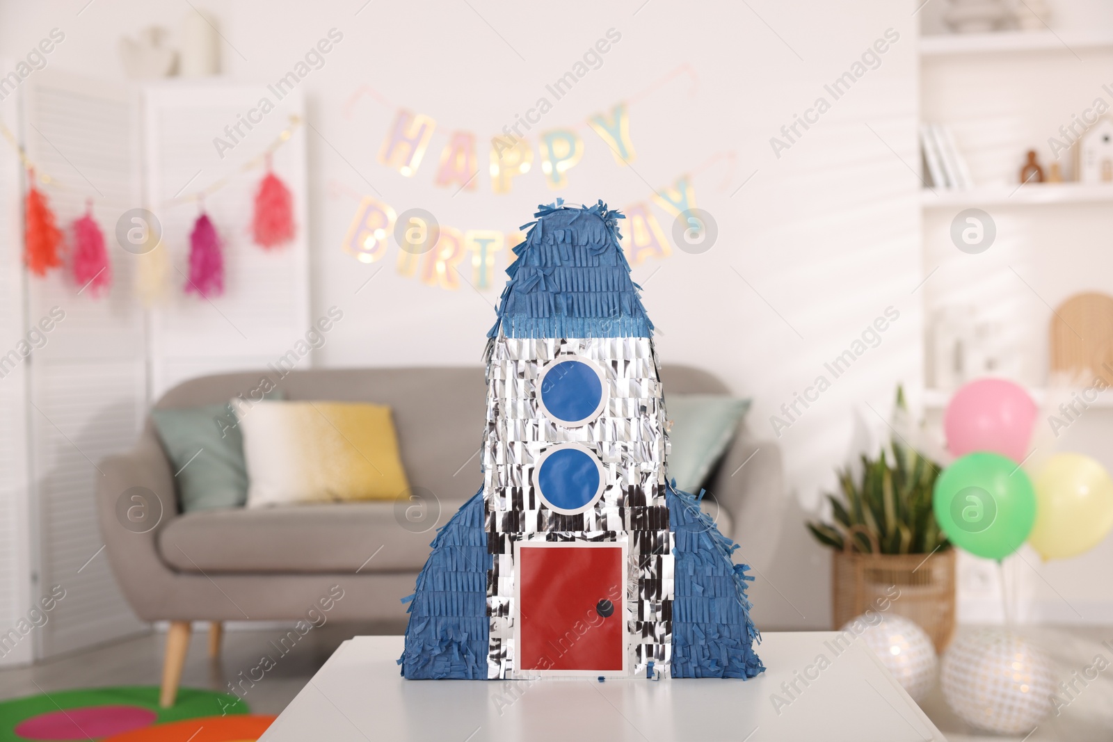 Photo of Bright pinata in shape of rocket on table in festive decorated room