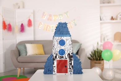 Photo of Bright pinata in shape of rocket on table in festive decorated room