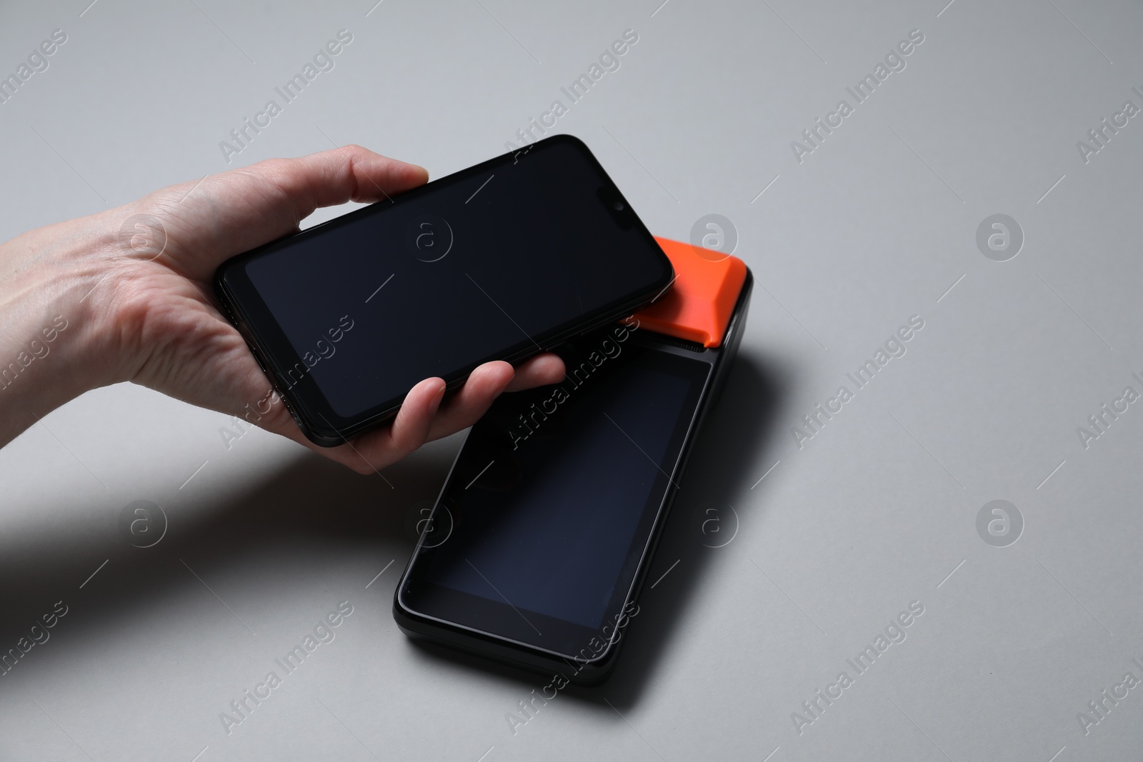 Photo of Woman with smartphone using payment terminal on grey background, closeup