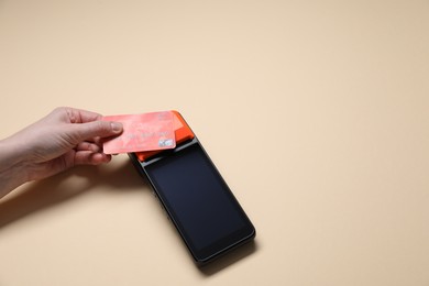 Photo of Woman with credit card using payment terminal on beige background, above view. Space for text