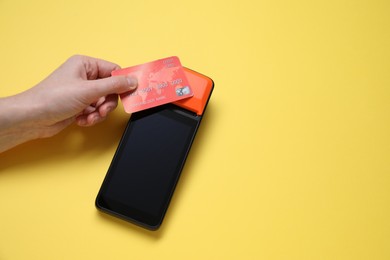 Photo of Woman with credit card using payment terminal on yellow background, top view. Space for text