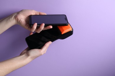 Photo of Woman with smartphone using payment terminal on violet background, closeup. Space for text