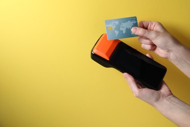 Photo of Woman with credit card using payment terminal on yellow background, closeup. Space for text