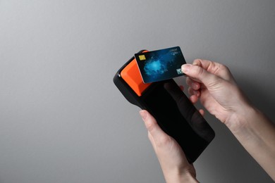 Photo of Woman with credit card using payment terminal on grey background, closeup. Space for text