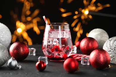 Photo of Tasty Christmas cocktail in glass, ice cubes and decor on black table against blurred lights, closeup