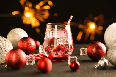 Photo of Tasty Christmas cocktail in glass, ice cubes and decor on black table against blurred lights, closeup