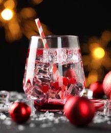 Photo of Tasty Christmas cocktail in glass, ice and decor on table against dark background with blurred lights, closeup