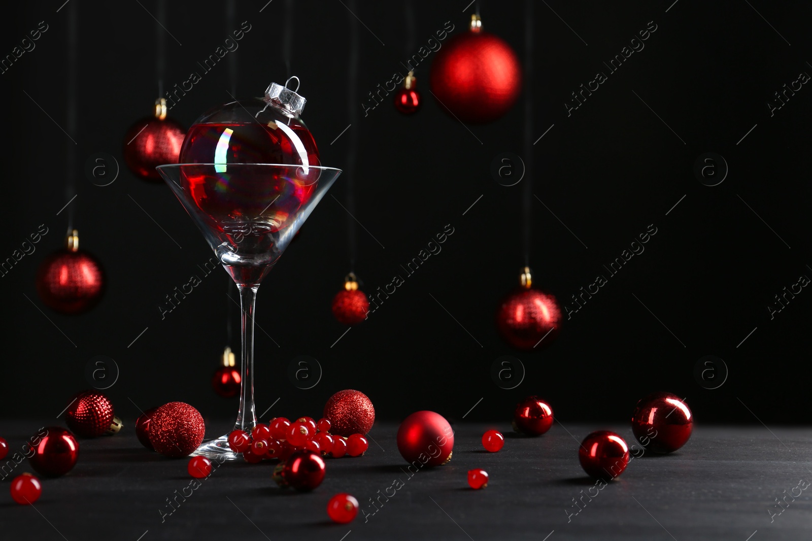 Photo of Creative presentation of Christmas cocktail in bauble and glass on black table