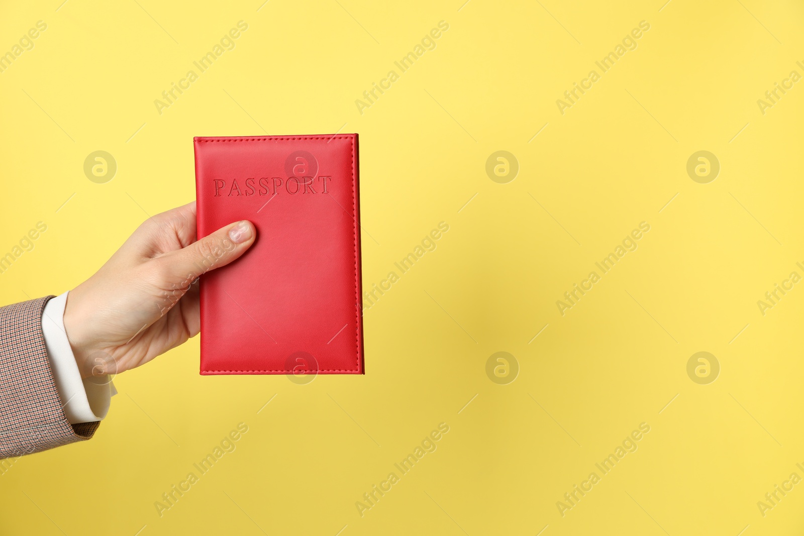 Photo of Woman holding passport in bright cover on yellow background, closeup. Space for text