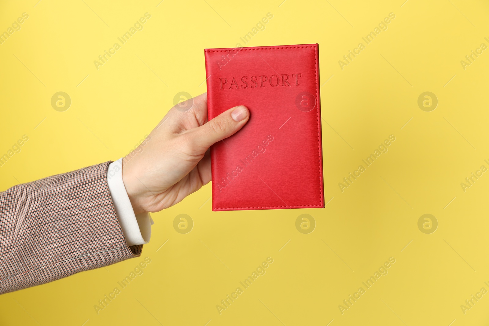 Photo of Woman holding passport in bright cover on yellow background, closeup