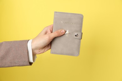 Photo of Woman holding passport in bright cover on yellow background, closeup