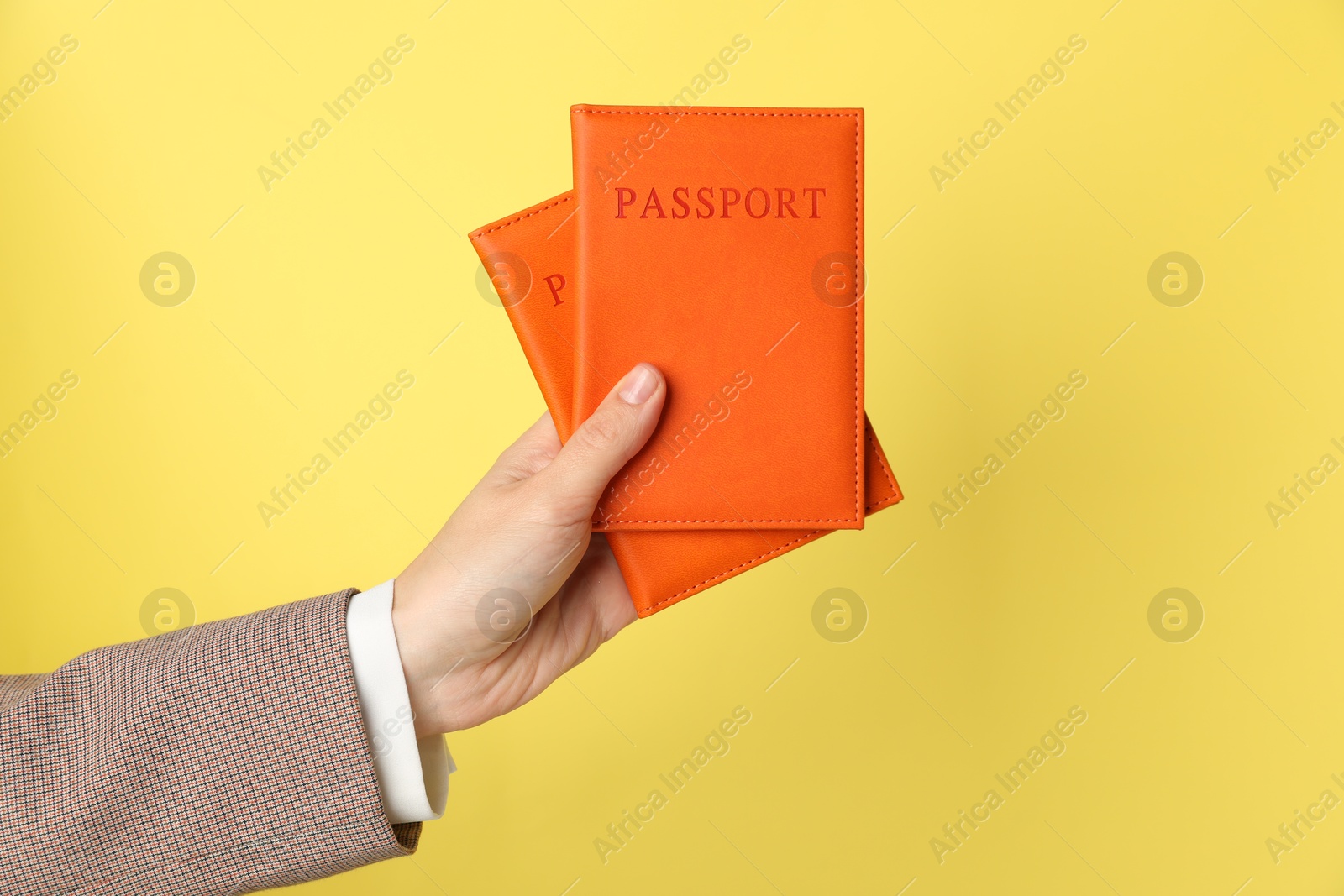 Photo of Woman holding passports in bright covers on yellow background, closeup