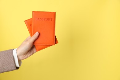 Photo of Woman holding passports in bright covers on yellow background, closeup. Space for text