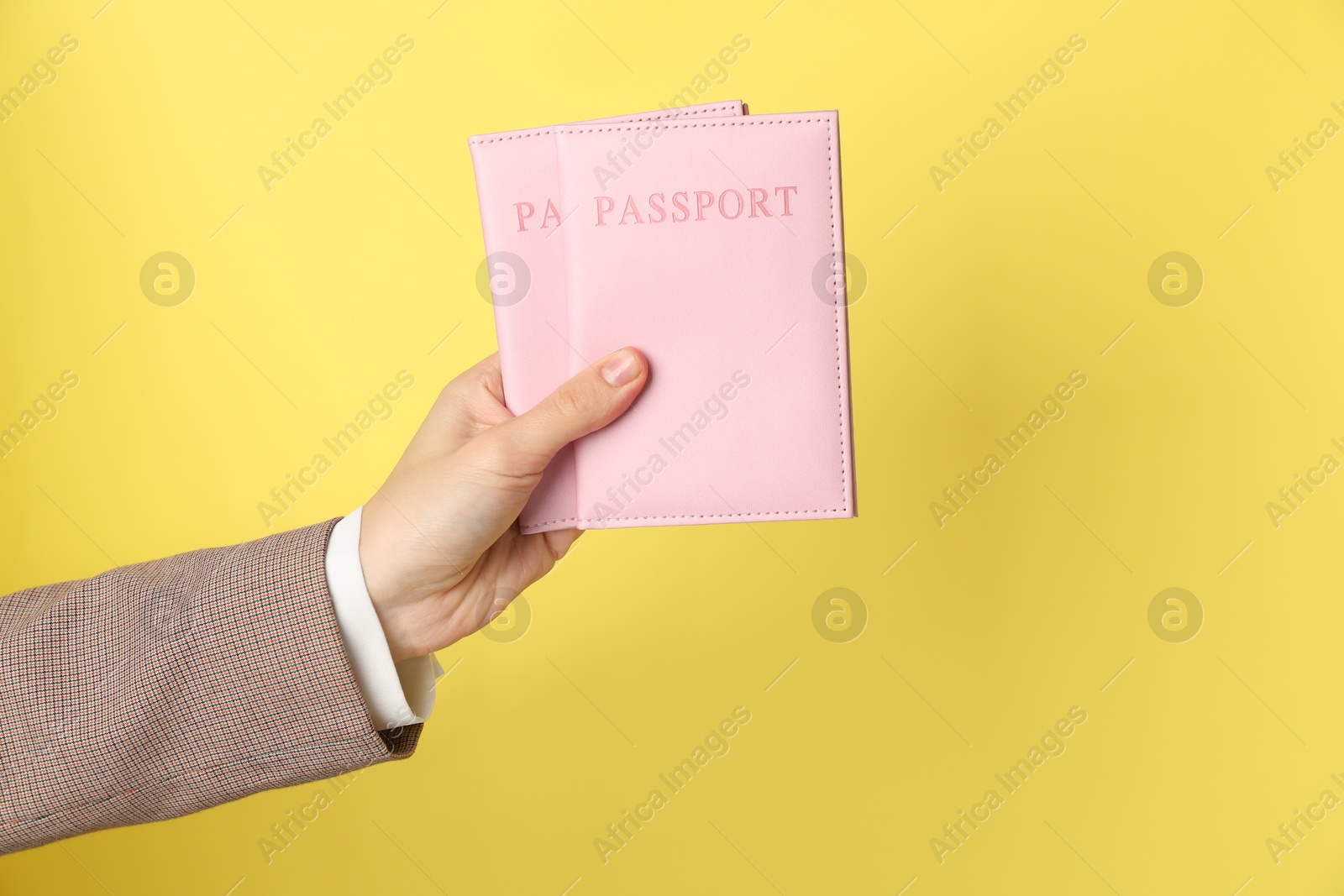 Photo of Woman holding passports in bright covers on yellow background, closeup. Space for text