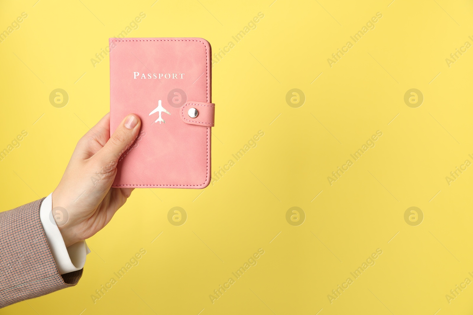 Photo of Woman holding passport in bright cover on yellow background, closeup. Space for text