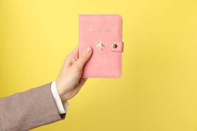 Photo of Woman holding passport in bright cover on yellow background, closeup. Space for text