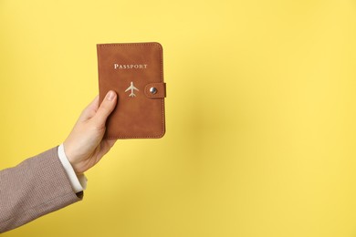 Photo of Woman holding passport in bright cover on yellow background, closeup. Space for text