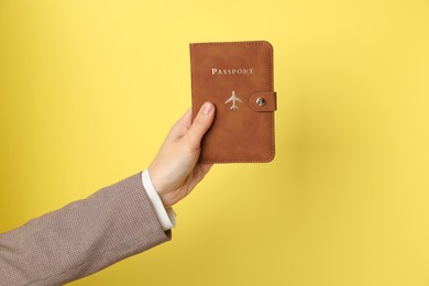 Photo of Woman holding passport in bright cover on yellow background, closeup