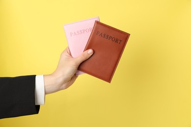 Photo of Woman holding passports in bright covers on yellow background, closeup. Space for text