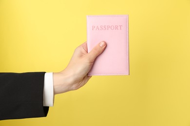 Photo of Woman holding passport in bright cover on yellow background, closeup. Space for text