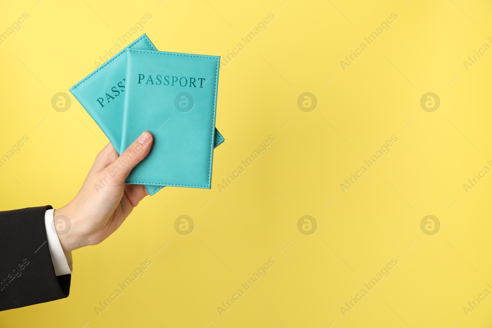 Photo of Woman holding passports in bright covers on yellow background, closeup. Space for text