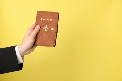 Photo of Woman holding passport in bright cover on yellow background, closeup. Space for text